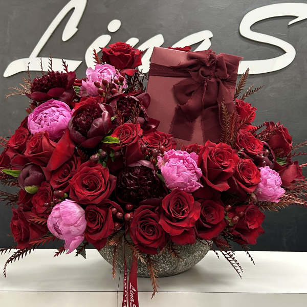 Red and pink rose arrangement in a round vase with a gift box