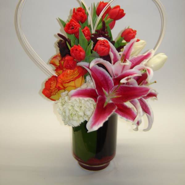 Red tulips and pink lilies in a dark vase with heart-shaped wire handles