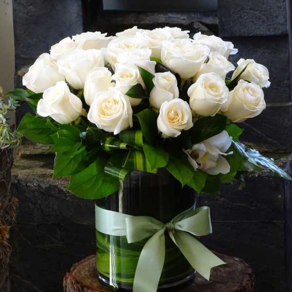 White roses arranged in a glass vase with a pale green ribbon