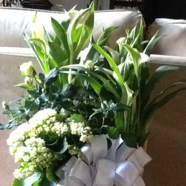 White floral arrangement in a wicker basket with a white ribbon