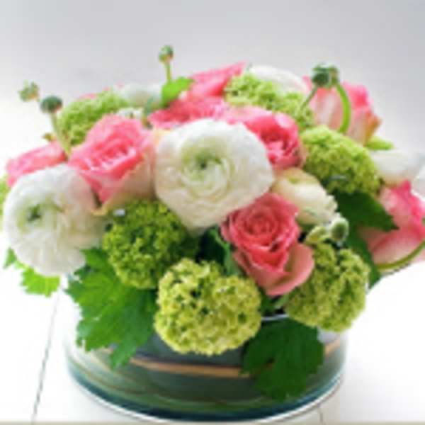 Low round arrangement of pink roses, white ranunculus, and green blooms in a clear glass bowl vase
