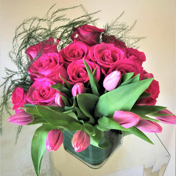 Compact arrangement of hot pink roses and tulips in a square glass vase