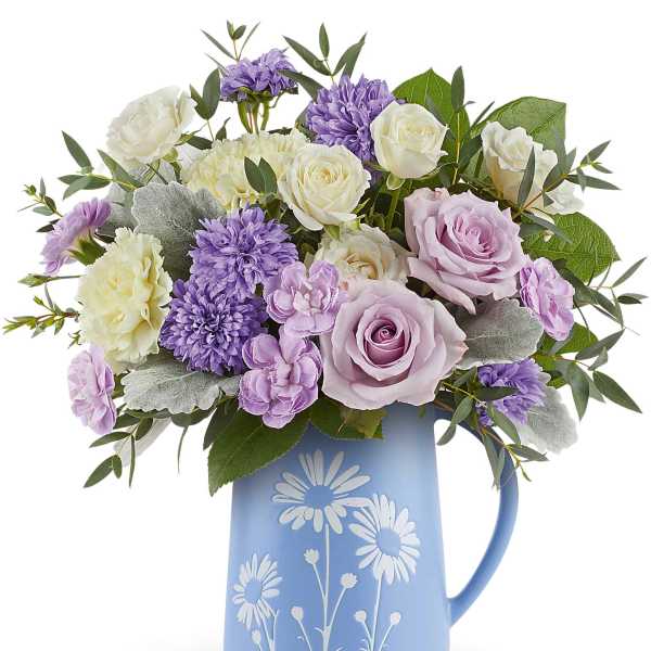 Lavender and white roses and mums arranged in a blue daisy-print ceramic pitcher