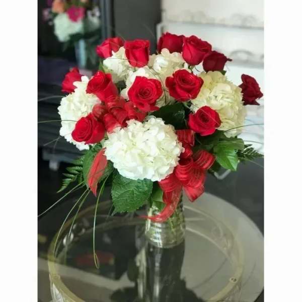 Vase arrangement of red roses and white hydrangeas with red ribbon accents