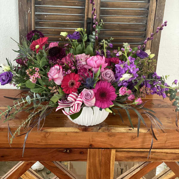 Low pink and purple flower arrangement with roses and gerberas in a white bowl with striped ribbon