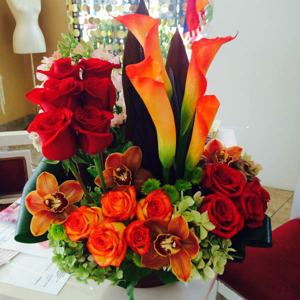 Arrangement of red roses, orange calla lilies, and orchids in a low container