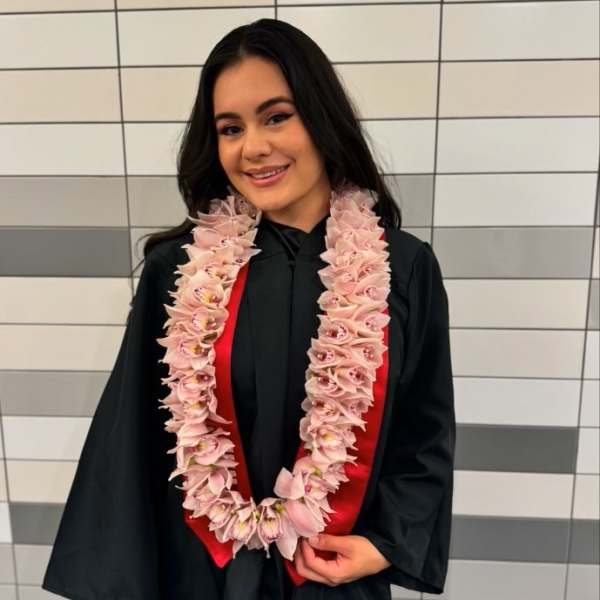 Woman in a graduation gown wearing a pink flower lei