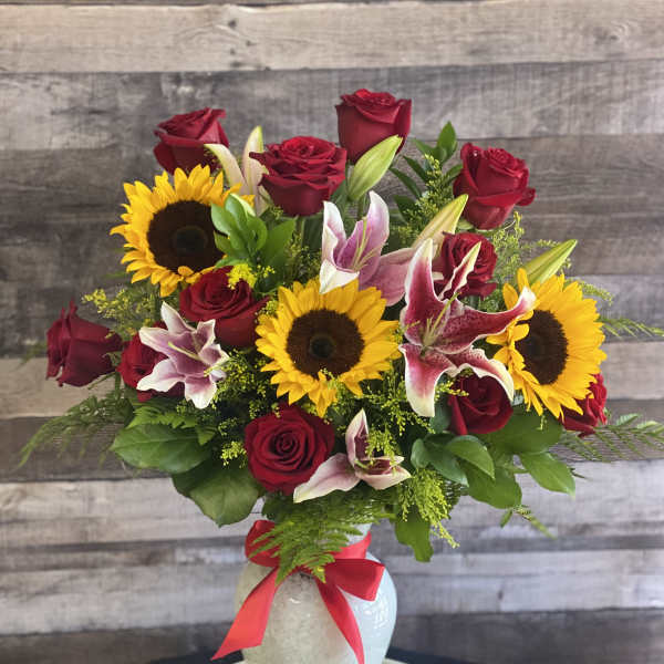 Bouquet of red roses, sunflowers, and lilies in a glass vase with a red ribbon