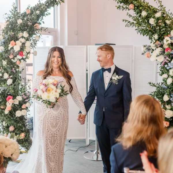 Bride and groom under a floral arch, with the bride holding a bouquet