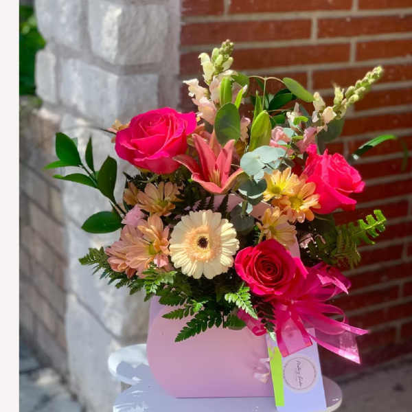 Pink floral arrangement in a purse-shaped container with a ribbon