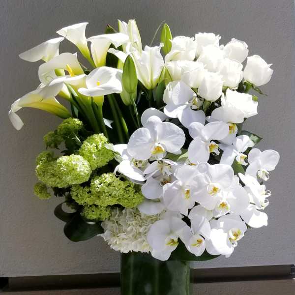 White calla lilies, roses, and orchids in a tall glass vase