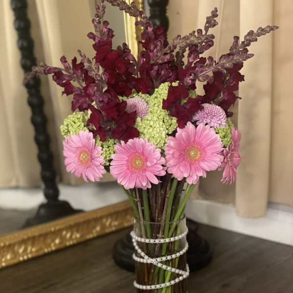 Pink gerbera daisies and burgundy snapdragons in a clear vase with pearl wrap