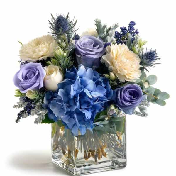 Blue and lavender floral arrangement in a clear square vase