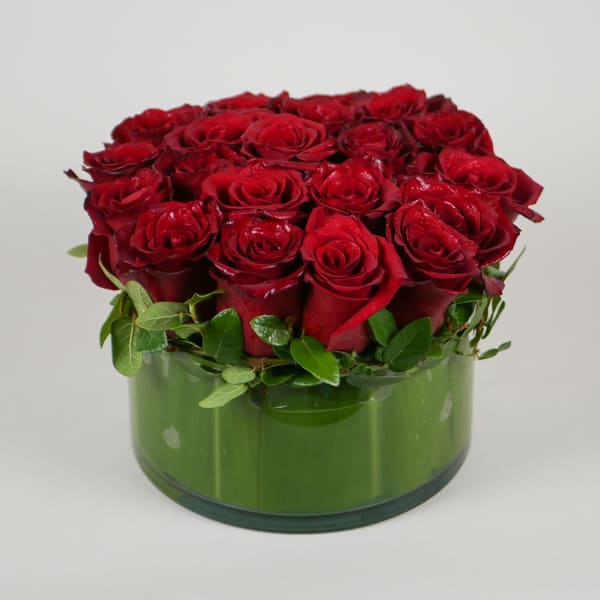 Red roses arranged in a round green glass vase