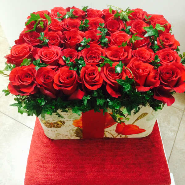 Red roses arranged in a rectangular gift box with ivy accents