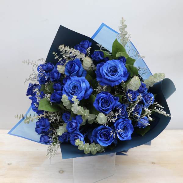 Hand-tied bouquet of vivid blue roses with silver eucalyptus in blue wrapping paper