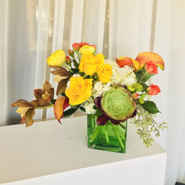 Mixed bouquet of yellow roses, orange calla lilies, and a green succulent in a glass vase