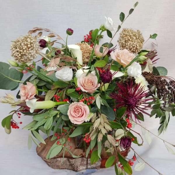 Rustic low arrangement with blush roses, dark red mums, berries, and a candle on a wood base.