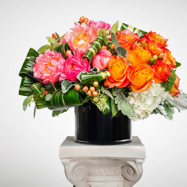 Bright pink peonies, orange roses, and white hydrangeas in a black cylinder vase