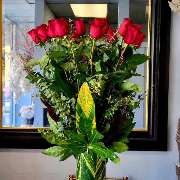 Tall vase arrangement of red roses with mixed greenery