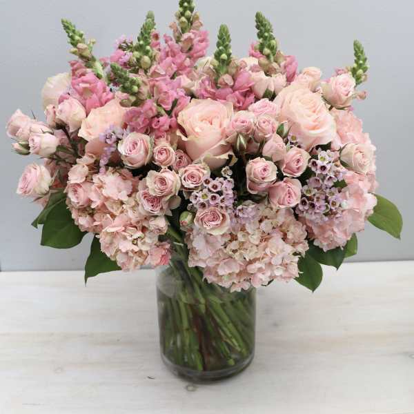 Large arrangement of soft pink roses, snapdragons, and hydrangeas in a clear glass vase.