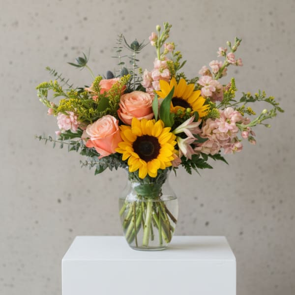 Bouquet of sunflowers and peach roses in a clear glass vase