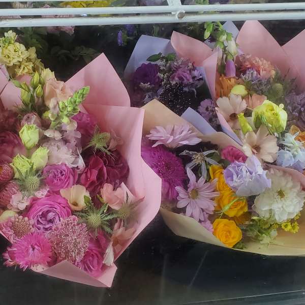 Assorted pastel-wrapped mixed flower bouquets arranged together in a cooler case