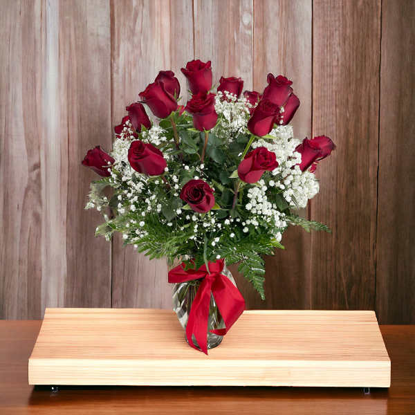 Red roses in a glass vase with white baby's breath and a red ribbon