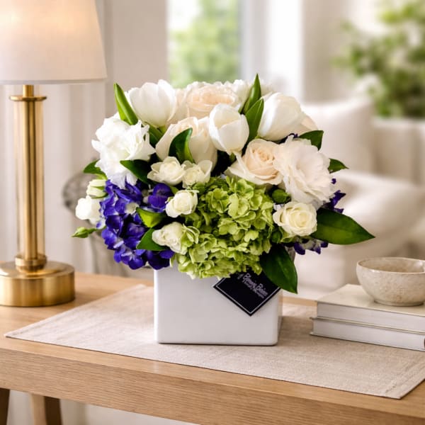 White and green floral arrangement in a square vase with purple blooms