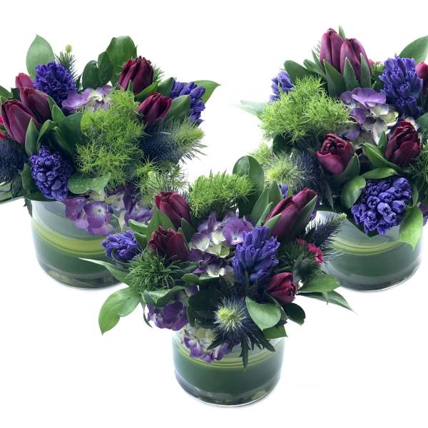 Three purple floral arrangements in green glass vases
