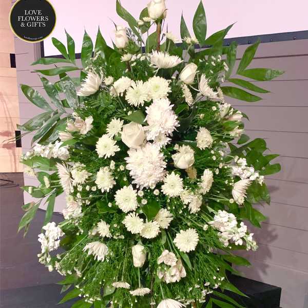 Tall standing spray of white roses and mums on a green easel.