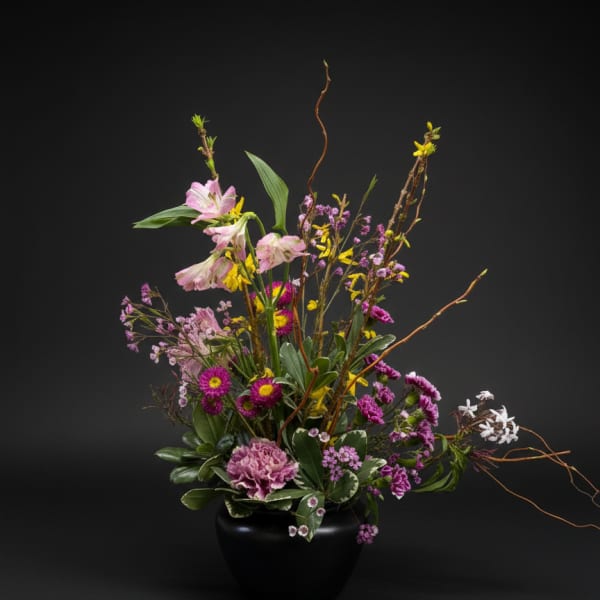 Tall mixed arrangement of pink, purple, yellow and white flowers in a black round vase