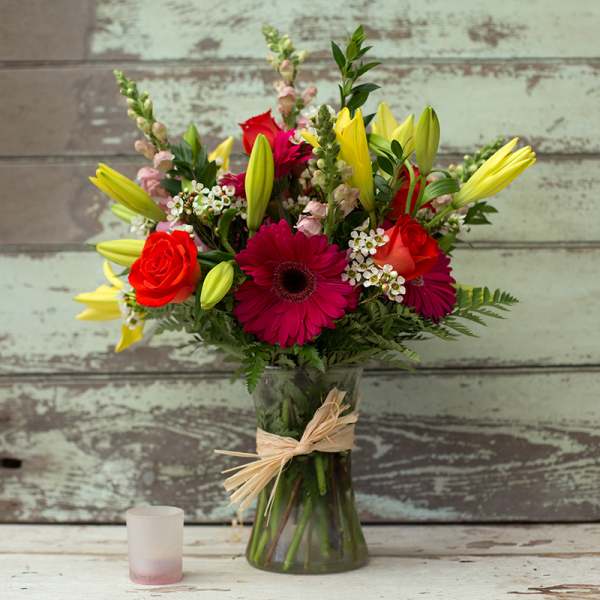 Mixed bouquet of red roses, pink gerbera daisies, and yellow lilies in a glass vase