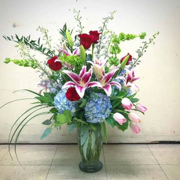 Tall vase arrangement with red roses, pink lilies, and blue hydrangeas
