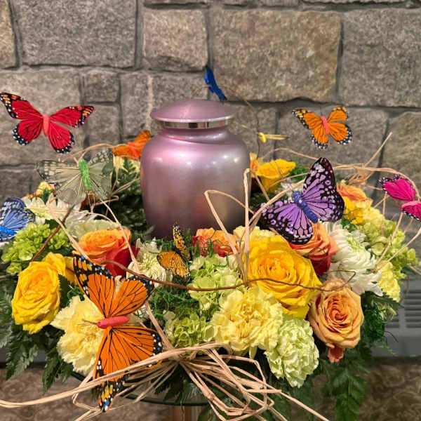 Butterfly-decorated floral arrangement around a pink urn