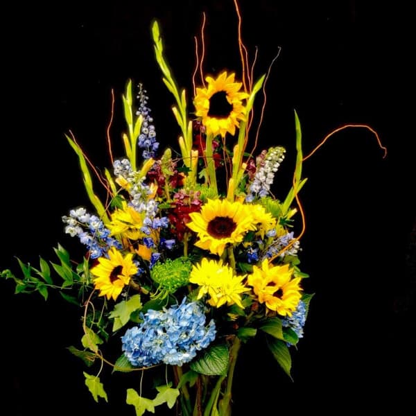 Tall bouquet of sunflowers and blue hydrangeas in a clear glass vase