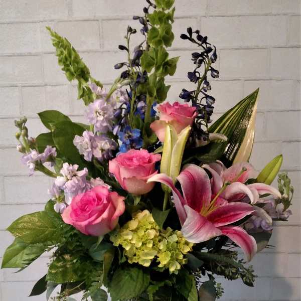 Pink roses and lilies in a clear glass vase with mixed purple blooms