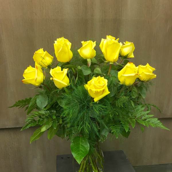 Yellow roses arranged in a clear glass vase with lush greenery