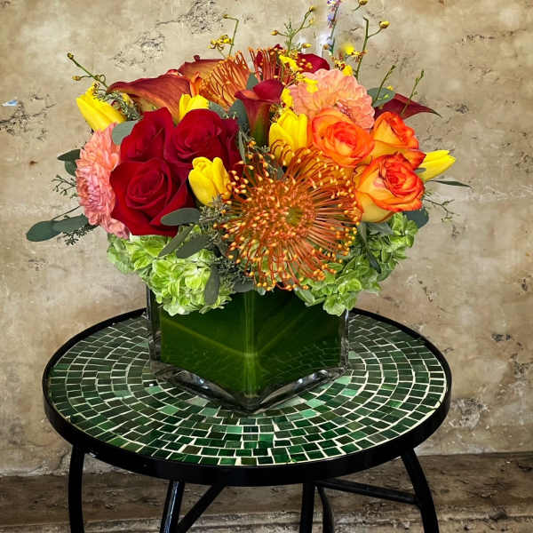 Colorful bouquet of roses, calla lilies, and hydrangeas in a square glass vase