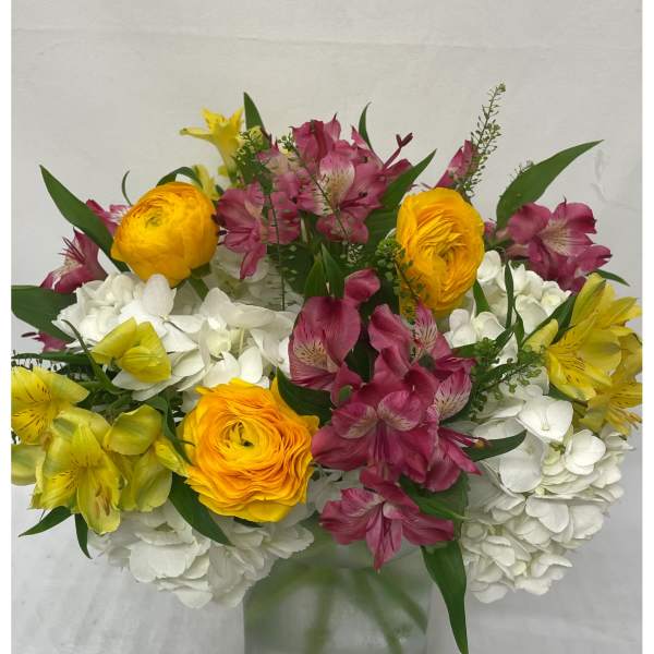 Mixed bouquet of white hydrangeas, yellow blooms, and pink alstroemeria in a clear glass vase