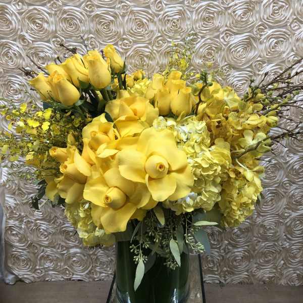 Yellow floral arrangement with roses and orchids in a glass vase