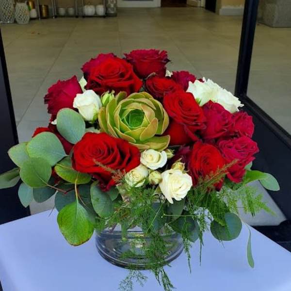 Low round arrangement of red and white roses with a green succulent in a clear glass bowl vase