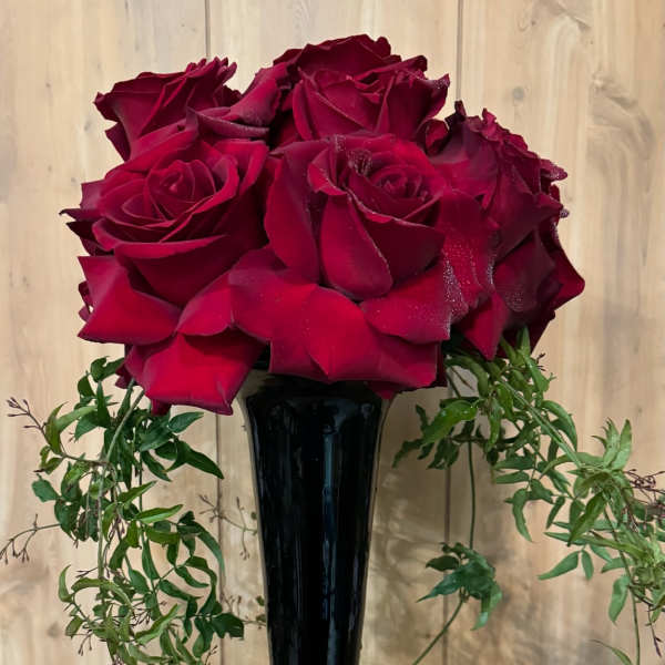 Red roses in a tall black vase with trailing greenery and a glittery heart