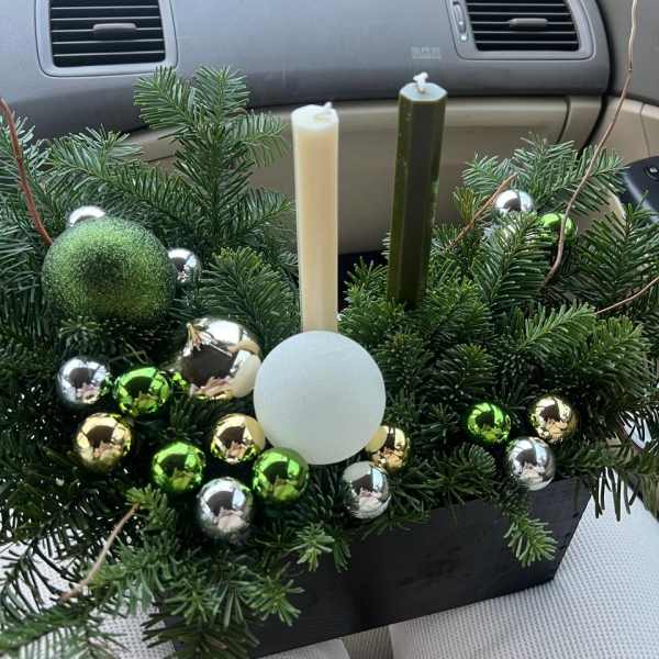 Evergreen holiday centerpiece with candles and shiny ornaments in a black container
