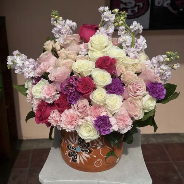Mixed pink, white, and purple roses in a decorative round container