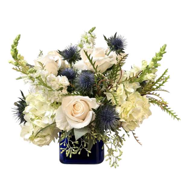 White roses and pale blooms in a blue vase with spiky blue thistles