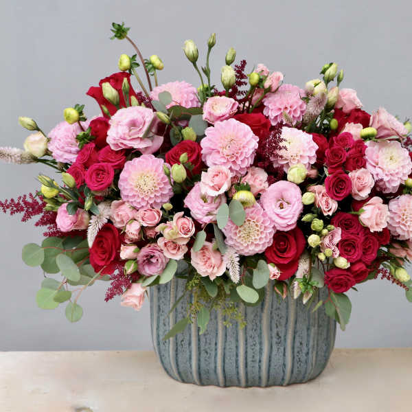 Lush pink and red flower arrangement in a textured blue ceramic container