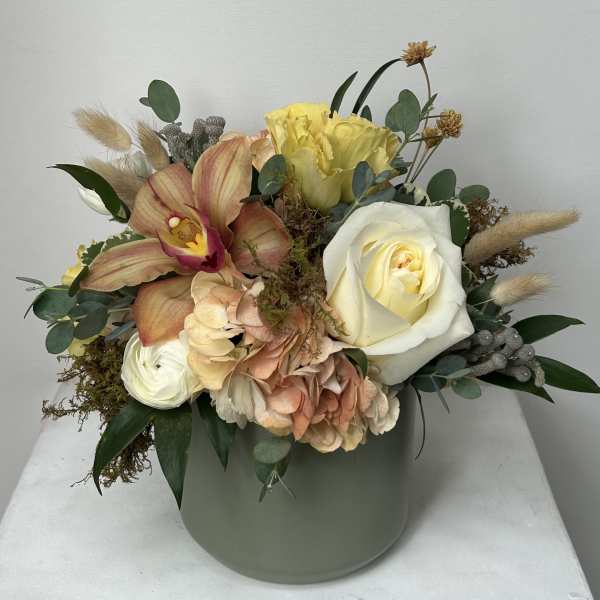 Mixed bouquet in a pale green vase with roses, orchids, hydrangea, and dried accents