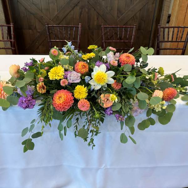 Long floral centerpiece with mixed blooms and trailing greenery on a table