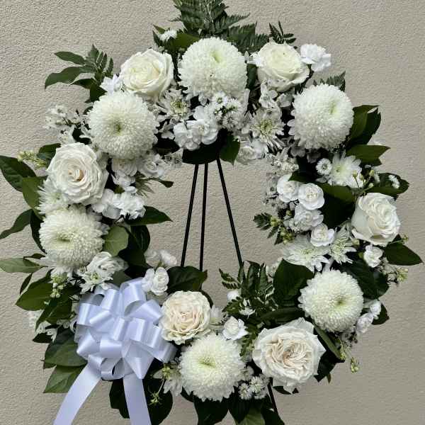 White floral wreath with roses and mums on a black stand
